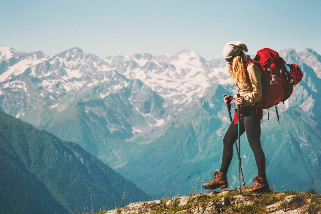 Turystka z plecakiem trekkingowym i kijkami idąca po górskiej ścieżce