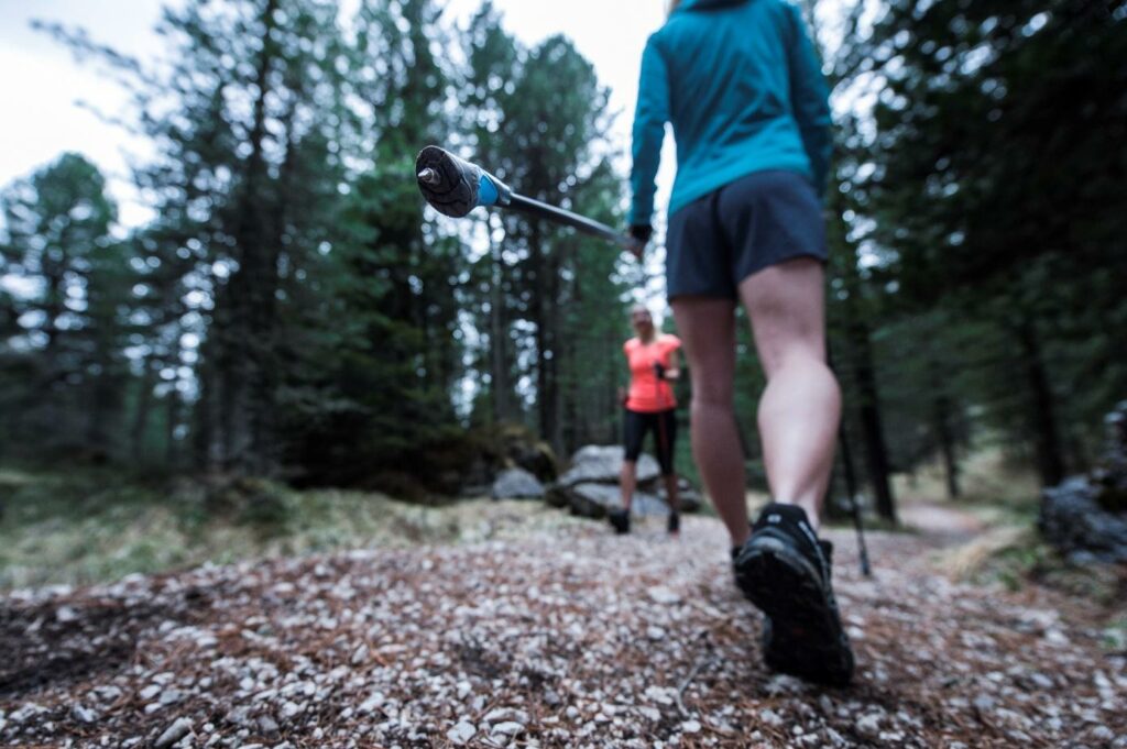 Metalowy grot w kijkach nordic walking trzymanych przez kobietę w czasie treningu w lesie