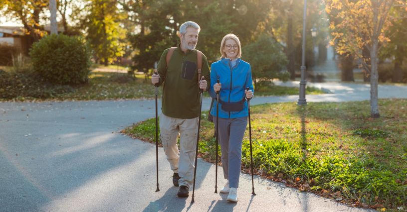Starsza para idzie z kijkami nordic walking parkową alejką w słoneczny jesienny dzień