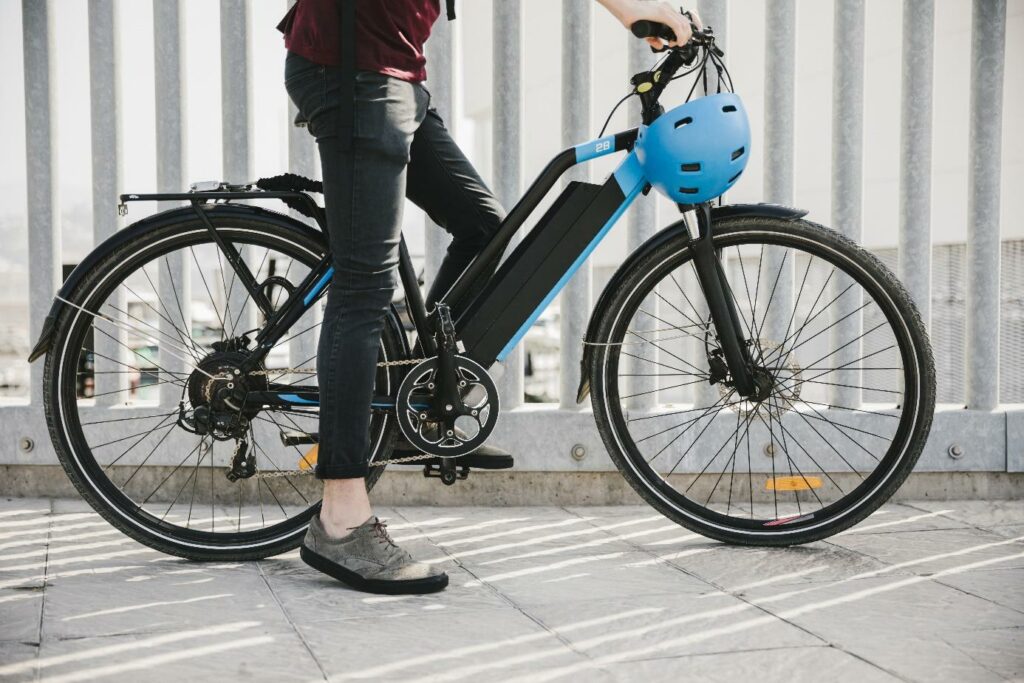Osoba stoi obok elektrycznego roweru zabezpieczonego kaskiem