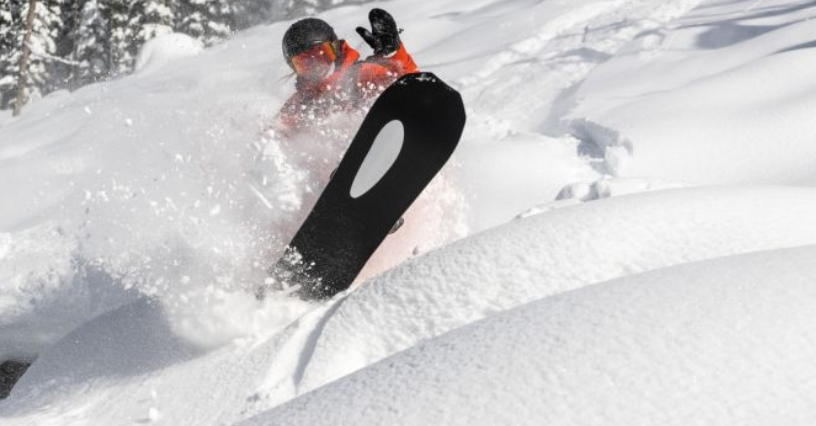 Sportowiec na snowboardzie zjeżdża z zaśnieżonego stoku