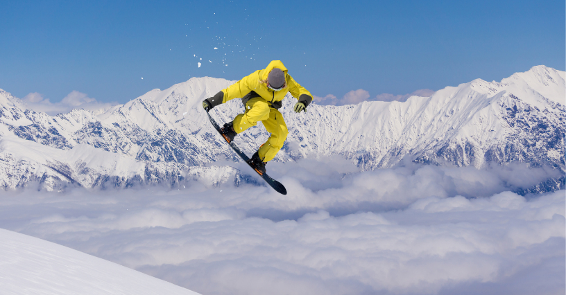 Snowboardzista w żółtym stroju wykonuje skok na tle ośnieżonych gór