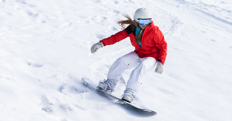 Kobieta na snowboardzie zjeżdża po ośnieżonym stoku