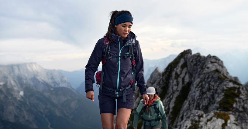 Kobieta w zaawansowanej odzieży outdoorowej wspina się górskim szlakiem