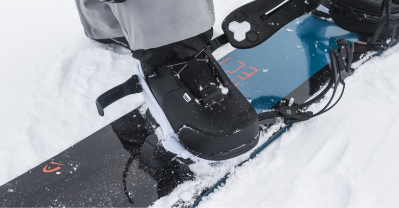 Mężczyzna zapina buty do snowboardu na śniegu