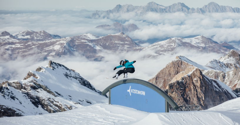 Snowboarder wykonuje skok na rampie wśród imponujących górskich widoków