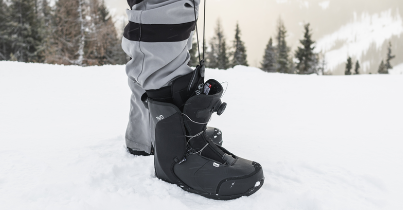 Mężczyzna w butach snowboardowych stoi na zaśnieżonym stoku