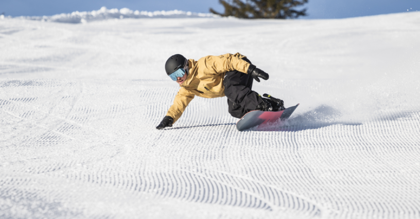 Snowboardzista wykonuje dynamiczny zjazd po świeżo przygotowanym stoku