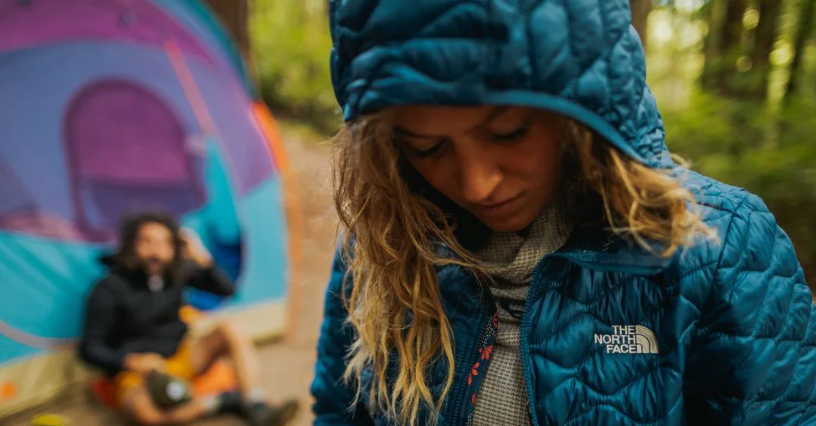 Kobieta w kurtce turystycznej North Face podczas biwakowania w lesie