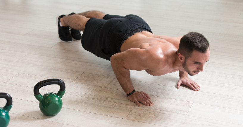 Mężczyzna ćwiczy pompki obok kettlebelli na drewnianej podłodze