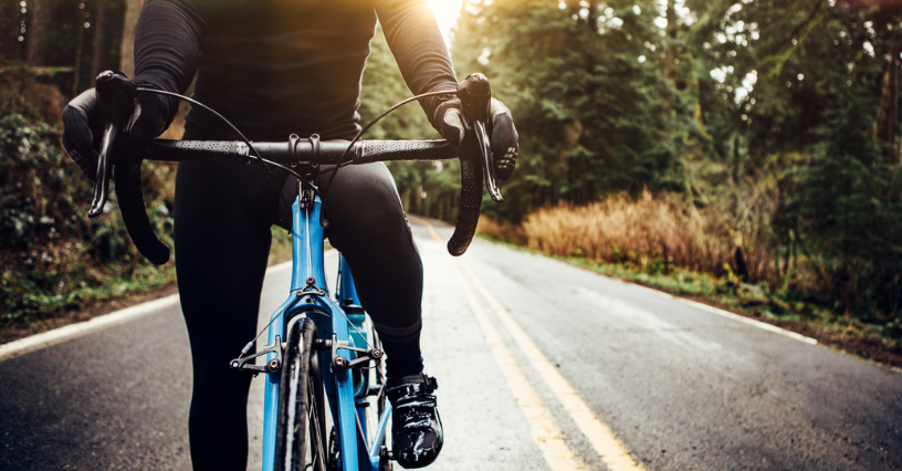 Rowerzysta na rowerze szosowym jedzie drogą asfaltową przez las