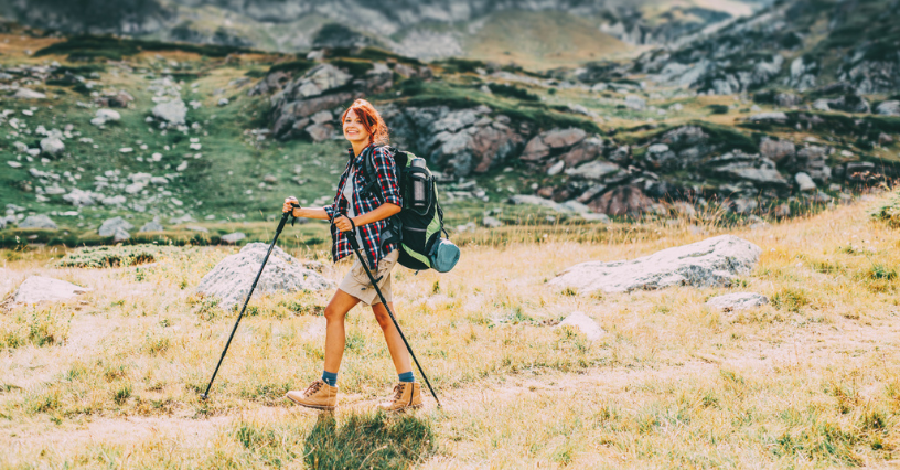 Kobieta z plecakiem i kijkami trekkingowymi idzie po górskiej łące