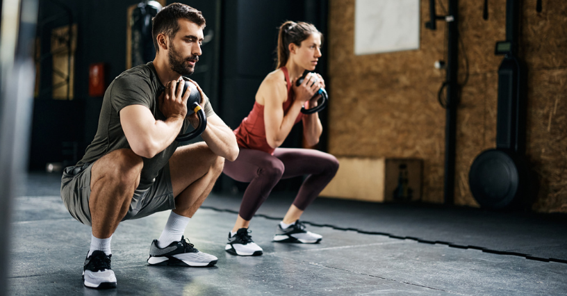 Mężczyzna i kobieta ćwiczą przysiady z kettlebellami na siłowni