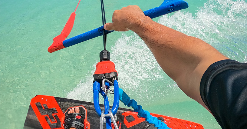 Osoba trzyma bar do kitesurfingu nad turkusową wodą