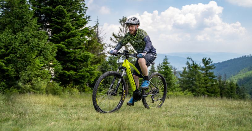 Mężczyzna w stroju i kasku rowerowym jadący po górskiej łące na rowerze MTB