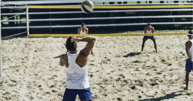Mężczyzna zagrywający piłkę z wyskoku w czasie meczu siatkówki plażowej