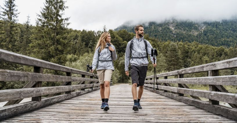 Para turystów z kijkami trekkingowymi przechodząca przez most nad rzeką w górach