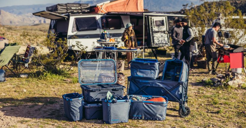 Organizery, torby, pojemniki i wózek z kolekcji Alpaca Gear Organization ustawione przed kamperem