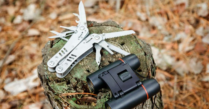 Srebrny multitool i lornetka leżące na pniu drzewa w lesie
