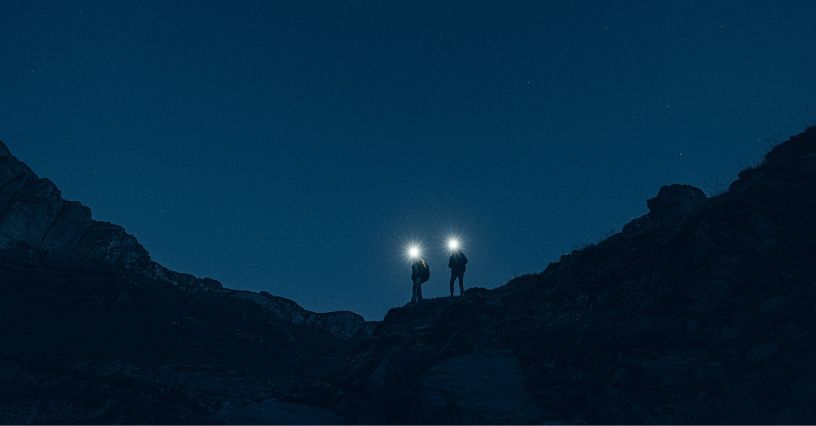 Turyści oświetlający sobie drogę latarkami czołowymi w czasie nocnej wyprawy po górach
