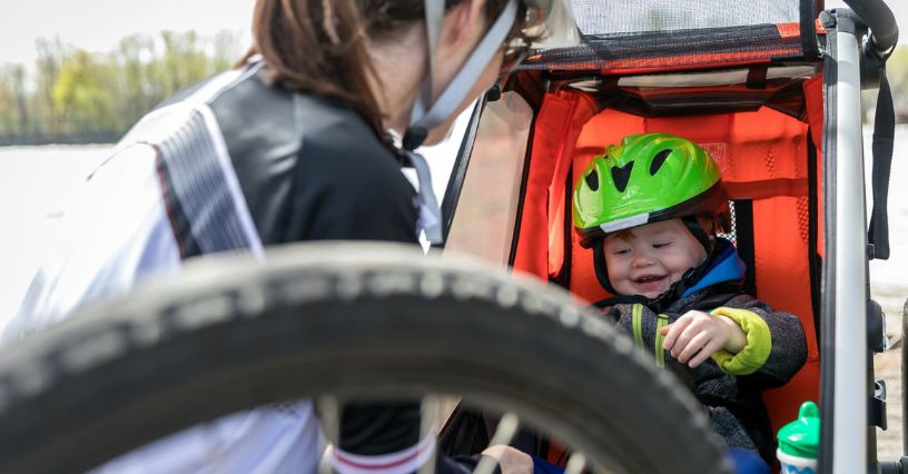 Dziecko w kasku w przyczepce rowerowej uśmiechające się do mamy