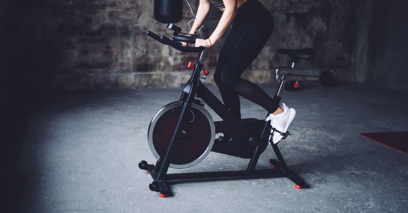 Kobieta jadąca na rowerze spinningowym w ciemnym pomieszczeniu
