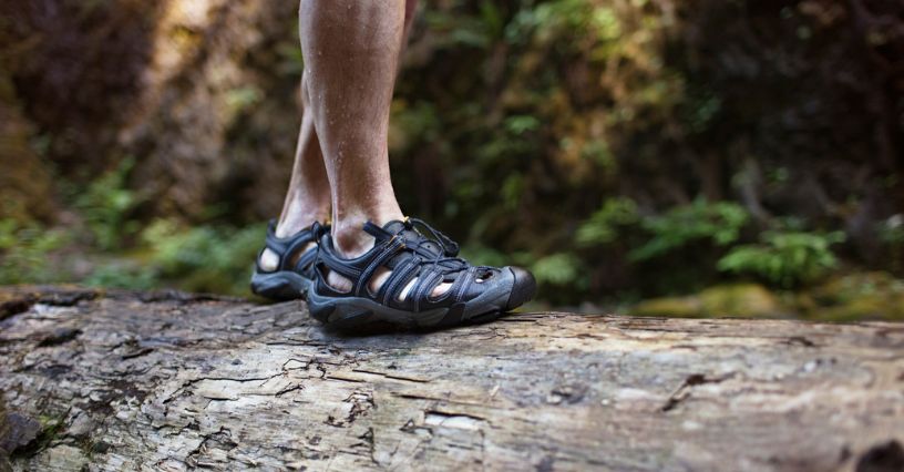 Mężczyzna idzie po pniu drzewa w sportowych sandałach trekkingowych